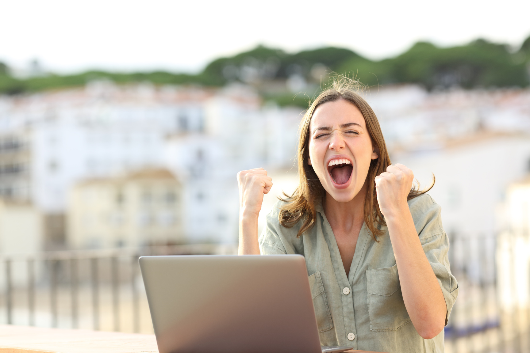 Excited woman celebrating with laptop in a balcony